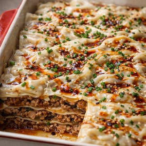 May include: A baked dish with layers of pasta, ground meat, and sauce, topped with sesame seeds and chopped green onions. The dish is in a rectangular baking dish with red accents, and steam rises from it.