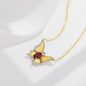 May include: A gold chain necklace featuring a butterfly pendant. The butterfly has yellow textured wings, a central oval-shaped red gemstone, and silver-toned edges accented with small clear stones along the wing borders.