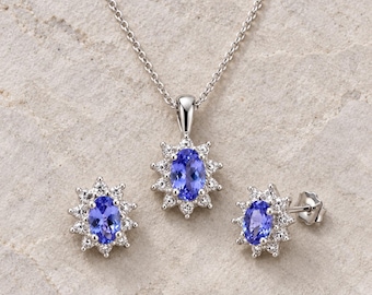 May include: A jewelry set consisting of a pendant necklace and matching stud earrings. Each piece features a central oval-cut blue gemstone surrounded by a halo of small white stones, all set in a polished silver-tone metal finish.