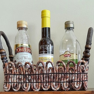 May include: A decorative basket holding three bottles of gourmet red wine vinegar, olive oil, and balsamic vinegar. The basket has woven sides and handles. The bottles have gold and yellow caps and labels.