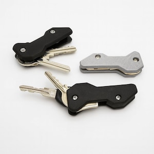 Puede incluir: Tres organizadores de llaves en negro y gris. Cada organizador contiene varias llaves, con un diseño compacto. Los organizadores están hechos de un material mate y asegurados con pequeños tornillos. Las llaves son plateadas.