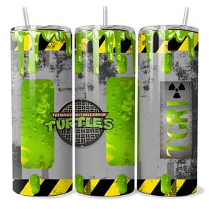 May include: A stainless steel tumbler featuring a Teenage Mutant Ninja Turtles design. The tumbler has a gray background with yellow and black hazard stripes, green slime drips, and the word "TCRI". Includes a straw.