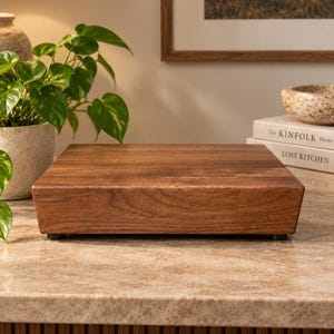 May include: A rectangular wooden riser with a smooth, dark brown grain finish. The platform features beveled edges and is supported by small, dark, circular feet at each corner, providing a stable, elevated surface for display purposes.