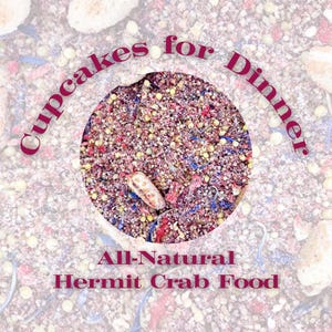 May include: A circular view of a dry, textured mixture of all-natural hermit crab food containing small grains, dried red fruit pieces, and blue flower petals. The text Cupcakes for Dinner and All-Natural Hermit Crab Food is printed in dark red.