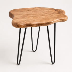 May include: A side table featuring a natural, irregular-shaped light brown wood slab top with visible grain patterns and knots. The tabletop is supported by three slender, black metal hairpin legs that extend outward from the center base.