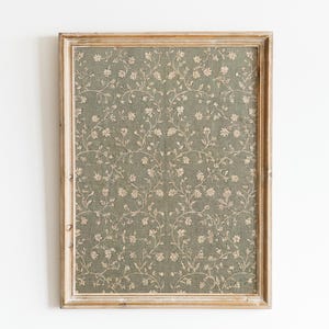 May include: A framed artwork with a floral design. The artwork has a muted green background with a repeating pattern of beige flowers and vines. The frame is made of light, distressed wood. The dimensions are in centimetres.