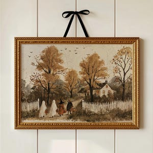 May include: A rectangular framed print featuring a landscape painting of four figures in costumes walking toward a house. The scene includes golden autumn trees, a white picket fence, and a black ribbon tied in a bow at the top of the gold frame.