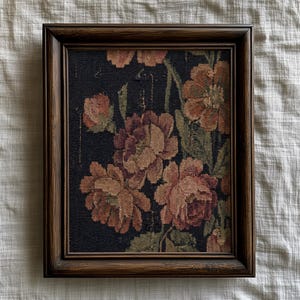 Puede incluir: Un tapiz floral enmarcado con grandes flores melocot&oacute;n y burdeos sobre un fondo oscuro. Las flores tienen hojas y tallos verdes. El marco es de madera marr&oacute;n oscuro.