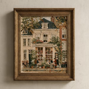 May include: A framed art print depicting a multi-storey building with a storefront labelled the independent bookshop. The scene features large windows filled with books, potted plants, bicycles, and figures standing outside on the pavement.