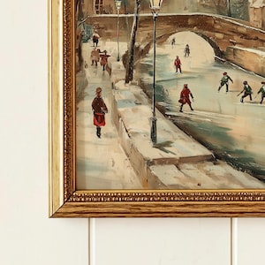 May include: A framed oil painting shows a winter scene with figures on a snowy path and bridge. The artwork features a bridge arching over a frozen waterway, with people in coats and hats. The painting has a vintage aesthetic, with a gold frame.