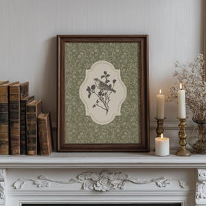 May include: A framed print featuring a detailed illustration of a bird perched on a flowering branch. The artwork is set against a green floral patterned background and framed in dark wood. The print is displayed on a white mantelpiece with candles and books.