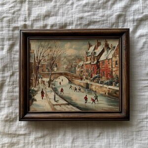 May include: A framed vintage painting shows a winter scene with a bridge, buildings, and figures ice skating. The artwork has a brown wooden frame and a muted colour palette, with snow-covered rooftops and a frozen waterway.