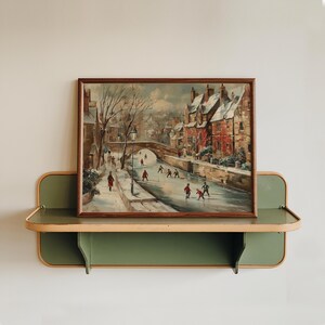 May include: A framed vintage painting showing a winter scene with people ice skating on a frozen river. The artwork, in a brown wooden frame, is displayed on a green and beige shelf. The painting features a bridge and buildings.