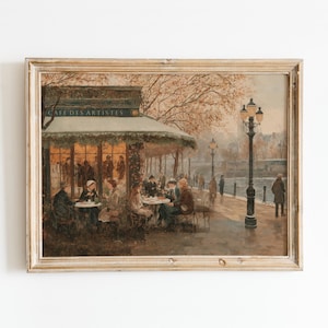 以下が含まれることがあります： 額縁に入ったヴィンテージプリントは、パリのカフェのシーンを描いています。「CAFE DES ARTISTES」の文字が入り口の上にあり、カフェの外のテーブルに座っている人々が描かれています。 ランプポストのある冬の風景です。