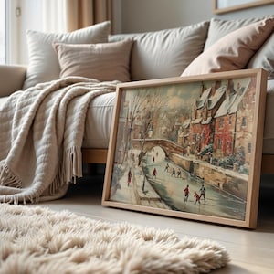 May include: A framed landscape painting of a winter scene with a bridge and figures, in a light wooden frame. The artwork is on a wooden floor. A beige rug and sofa with cushions are in the background. The painting is in a light wooden frame.