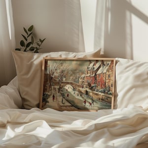 May include: A framed painting showing a winter scene of a European town with a bridge over a waterway. The buildings are red brick with snow-covered roofs. Figures are walking and ice skating. The frame is light brown.