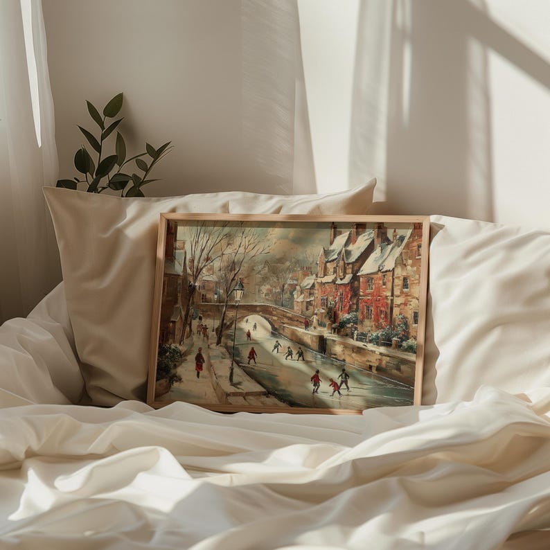 May include: A framed painting showing a winter scene of a European town with a bridge over a waterway. The buildings are red brick with snow-covered roofs. Figures are walking and ice skating. The frame is light brown.