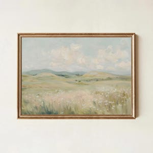 Puede incluir: Pintura al óleo de un paisaje sereno con colinas, un campo de flores silvestres y un cielo nublado. La obra de arte está enmarcada en un marco dorado y ornamentado. La paleta de colores es suave, con verdes, azules y blancos.
