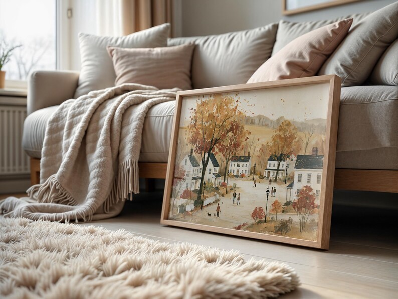 Puede incluir: Una l&aacute;mina de arte enmarcada de forma rectangular que presenta una ilustraci&oacute;n al estilo acuarela de una escena callejera de un barrio durante el oto&ntilde;o. La imagen muestra casas blancas, &aacute;rboles altos con follaje naranja y marr&oacute;n.