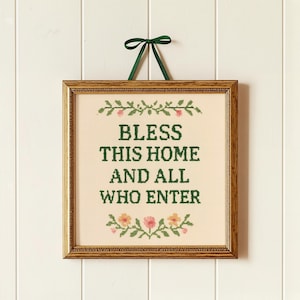 Pode incluir: Um bordado em ponto cruz quadrado numa moldura dourada com uma fita verde escura para pendurar. O tecido creme apresenta o texto verde escuro "BLESS THIS HOME AND ALL WHO ENTER" ladeado por motivos florais bordados em rosa, amarelo e verde.