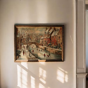 May include: A framed painting shows a winter scene with a frozen river. People are ice skating and walking along the banks. Buildings with red roofs line the river, and a bridge arches in the background. The frame is gold.
