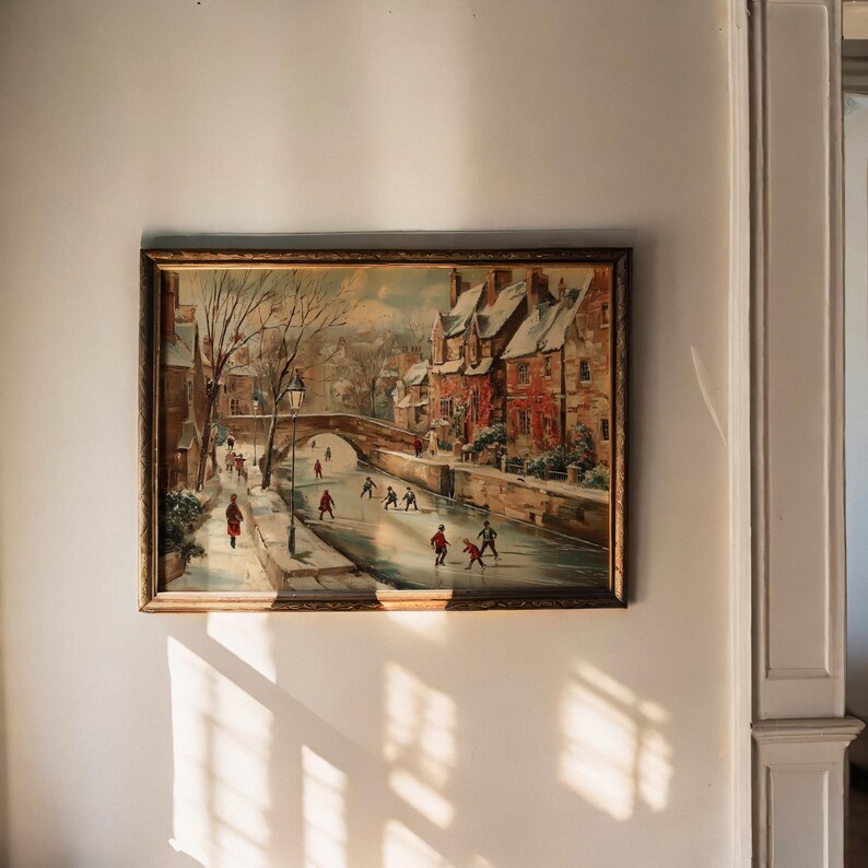 May include: A framed painting shows a winter scene with a frozen river. People are ice skating and walking along the banks. Buildings with red roofs line the river, and a bridge arches in the background. The frame is gold.