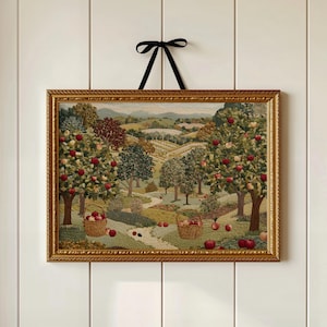 May include: A framed tapestry showing an orchard scene with apple trees bearing red fruit. Two baskets of apples are on the ground. The tapestry is in a gold frame and is suspended by a black ribbon.