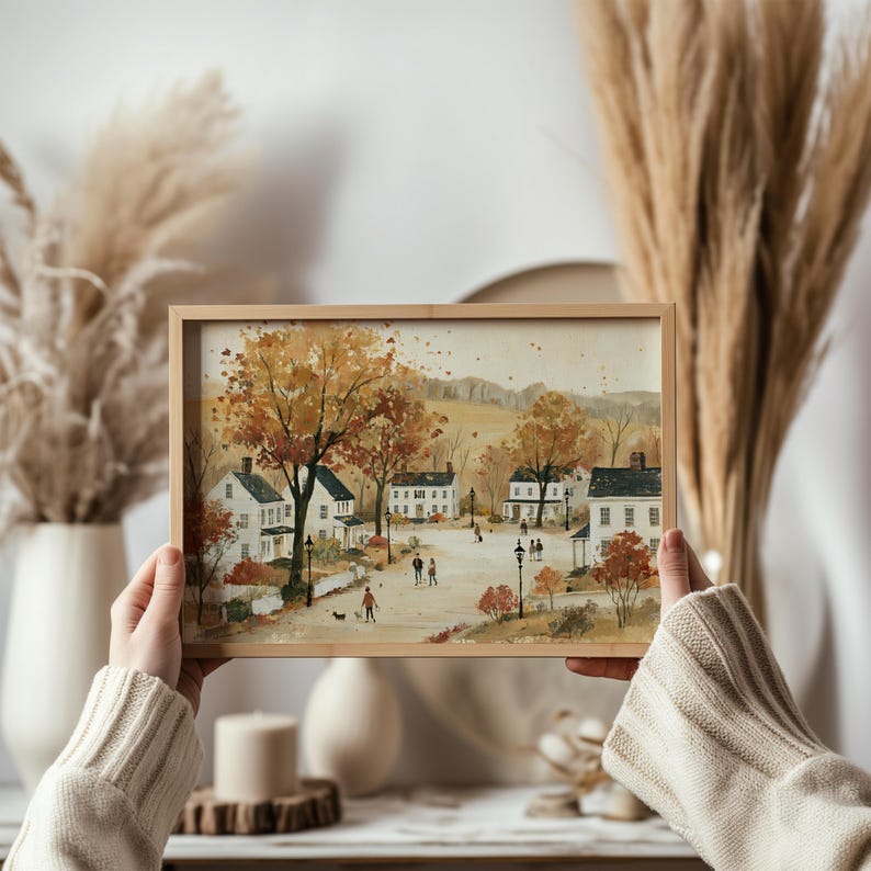 Puede incluir: Una pintura en acuarela enmarcada de forma rectangular que representa una escena callejera de un pueblo peque&ntilde;o en oto&ntilde;o. La obra muestra casas blancas, &aacute;rboles con follaje naranja y amarillo, farolas y figuras peque&ntilde;as.