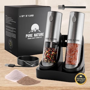 Puede incluir: Un juego de molinillos eléctricos de acero inoxidable con una base negra, un cable de carga y una caja con el texto "A Gift of Flavor" y "Pure Nature Premium Quality Grinder Set". Un molinillo contiene granos de pimienta, el otro sal rosa.