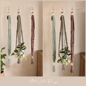 May include: Three macrame plant hangers in sage green, grey, and dusty rose, each featuring a wooden ring at the top and a knotted cord design. One hanger holds a potted plant with variegated green leaves. The text Atelier Libre Fil is visible.