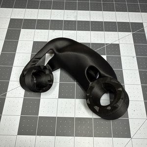 May include: A black, 3D-printed object with a curved design and two circular ends. The object has a smooth, matte finish and appears to be made of plastic. The ends have a textured pattern. The object is on a grey and white grid.