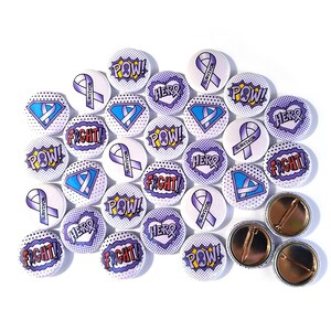 Puede incluir: Una colección de 20 botones redondos de color morado, blanco y azul con diferentes frases e imágenes. Las frases incluyen "POW!" "FIGHT!" "HERO" y "SURVIVOR". Las imágenes incluyen una cinta morada, un símbolo de superhéroe y un globo de diálogo de estilo cómic.