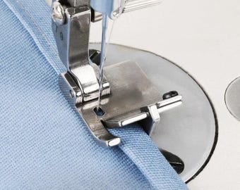 May include: Close-up of a sewing machine foot and needle in action, stitching light blue fabric. The metal components of the machine are in sharp focus, highlighting the precision of the sewing process. The fabric is being guided through the machine.