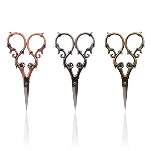 Può includere: Tre paia di forbici in metallo con manici decorati e a spirale. Il paio a sinistra è color rame, quello centrale è grigio metallizzato scuro e quello a destra è color ottone antico. Ogni paio presenta lame in acciaio appuntite e una vite.
