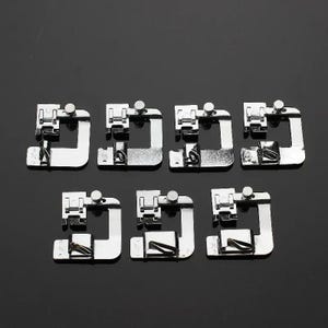 Puede incluir: Siete prensatelas plateados para máquina de coser, dispuestos sobre una superficie oscura. Cada prensatelas tiene forma rectangular con un borde curvo y un pequeño tornillo. Diseñados para diversas tareas de costura.