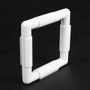 May include: A square embroidery hoop frame constructed from four white plastic tubes connected by corner joints. The frame features four straight side segments with integrated clips along the outer edges, designed to hold fabric taut for needlework projects.