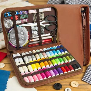 May include: A brown zipped sewing kit case containing a variety of colourful thread spools, a circular needle case, black scissors, safety pins, measuring tape, buttons, and various sewing tools held in place by elastic bands.