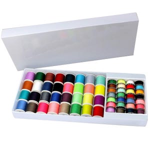 Puede incluir: Una caja de almacenamiento rectangular blanca que contiene una gran colección de carretes de hilo de coser en una amplia variedad de colores vibrantes. El conjunto incluye carretes más grandes en filas y una sección con carretes más pequeños.
