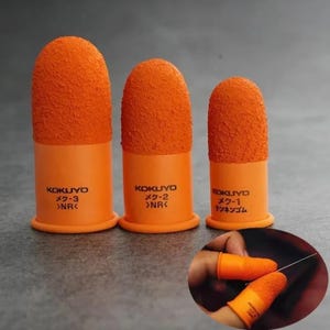 Puede incluir: Tres dediles de goma naranja de diferentes tamaños, cada uno con una punta texturizada y granulada y una base lisa. Los dediles llevan la marca KOKUYO y números de modelo. Un recuadro muestra los dediles colocados en las yemas de los dedos.