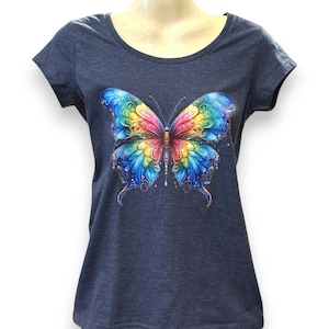 Puede incluir: Una camiseta azul oscuro con un diseño de mariposa colorido. La mariposa tiene detalles intrincados con tonos de azul, verde, amarillo, rosa y morado. La camiseta tiene cuello redondo y mangas cortas.