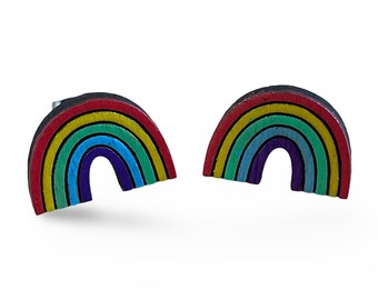 Op de afbeelding: Een paar regenboogkleurige houten oorbellen. Elke oorbel is gevormd als een regenboogvorm met rode, oranje, gele, groene, blauwe, indigo en violette strepen.