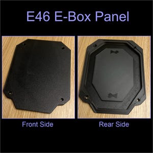 Può includere: Pannello E46 E-Box nero, lati anteriore e posteriore mostrati. La parte anteriore è un pannello rettangolare piatto con angoli arrotondati e tre fori. Il retro ha un design ottagonale rialzato con fori per viti.