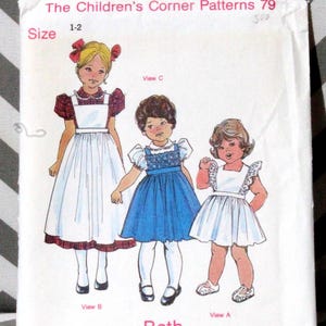 Puede incluir: Un patrón de costura vintage titulado "The Children's Corner Patterns 79" con ilustraciones de tres niñas con vestidos. El patrón es de talla 1-2 e incluye el nombre "Beth" y "An Elizabeth Travis Johnson Design."