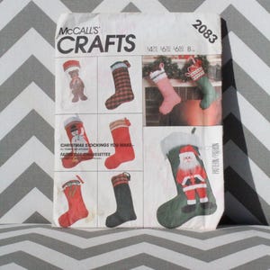 May include: A McCall's Crafts sewing pattern envelope, number 2083, featuring illustrations of various Christmas stockings. The white paper envelope displays multiple stocking designs, including a teddy bear, plaid, snowman, and Santa Claus motifs.