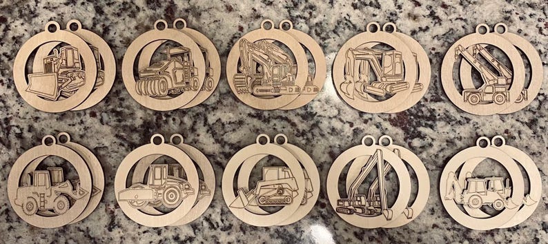 May include: A collection of ten wooden ornaments, each featuring a different construction vehicle design. The ornaments are circular with a cutout design of a bulldozer, excavator, and other heavy machinery. Each ornament has a small hole at the top for hanging.