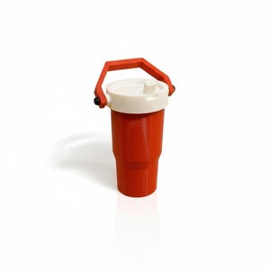 Puede incluir: Un vaso rojo con tapa blanca y asa roja. El vaso tiene forma cil&iacute;ndrica y un asa que se arquea sobre la parte superior. La tapa tiene una peque&ntilde;a abertura para beber. El vaso es probablemente de pl&aacute;stico.