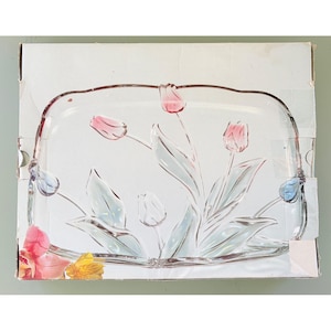 May include: A rectangular clear glass serving tray featuring an etched design of tulips with pink-tinted petals and green leaves. The tray is displayed on top of its original white cardboard packaging box which shows a floral graphic.