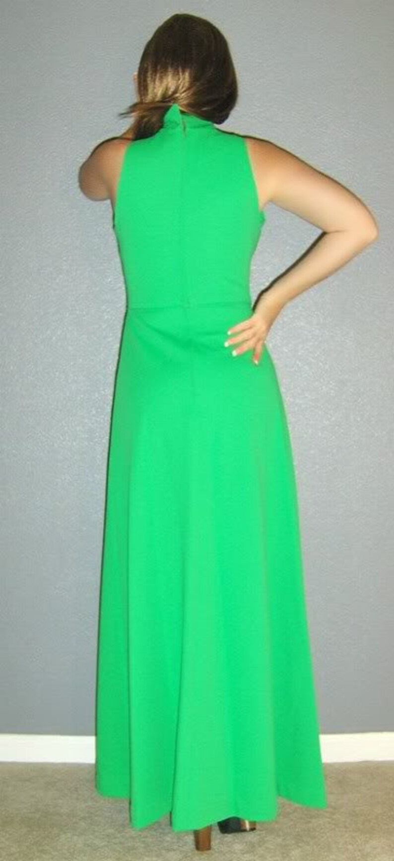 Puede incluir: Un vestido maxi verde brillante con cuello alto y sin mangas. El vestido tiene una silueta simple y elegante.