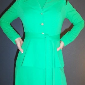 Puede incluir: Un vestido largo de manga larga, de color verde, con cuello alto, cierre de botones y cintur&oacute;n. El vestido tiene un corpi&ntilde;o ajustado y una falda fluida.