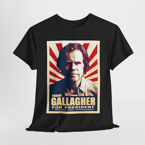 Puede incluir: Camiseta negra con un gráfico de un hombre y el texto "FRANK GALLAGHER FOR PRESIDENT" en azul y blanco. El diseño incluye un fondo a rayas rojas y blancas y las palabras "Absolutely, Wildly, Unapologetically".